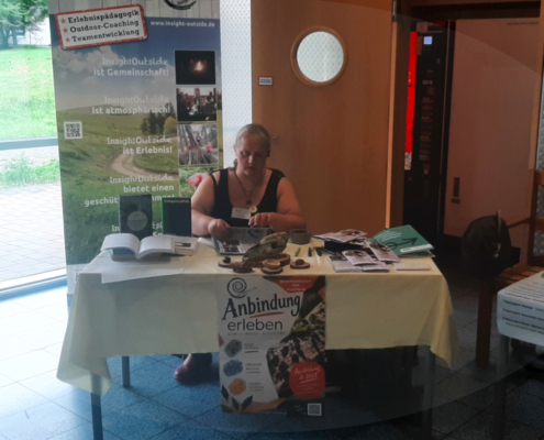 Frau sitzt an einem Messestand zum Thema Erlebnispädagogik und Lebendige Anbindung