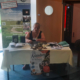 Frau sitzt an einem Messestand zum Thema Erlebnispädagogik und Lebendige Anbindung