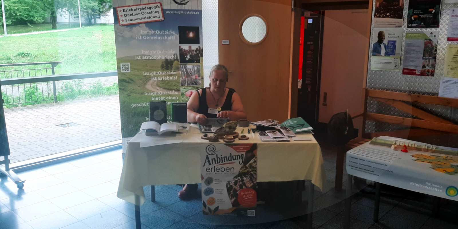 Blogeintrag ANU-Fachtag 04. Oktober 2026 Frau sitzt an einem Messestand zum Thema Erlebnispädagogik und Lebendige Anbindung
